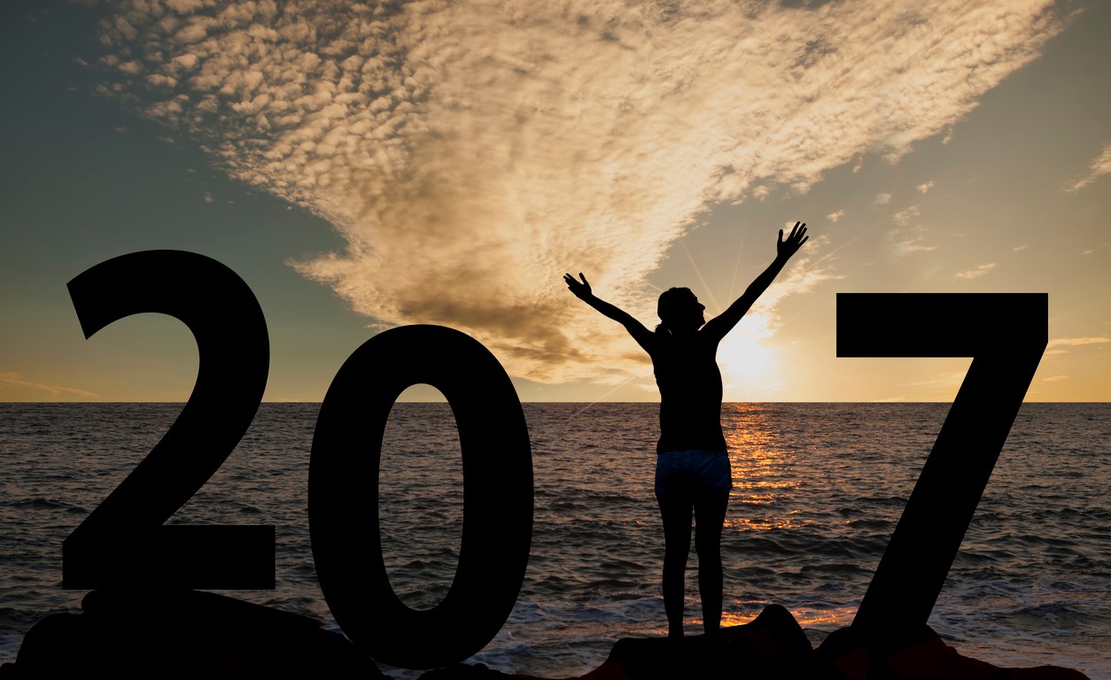 A person standing on the beach with arms raised waiting for the sunrise