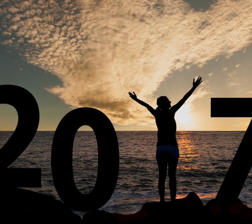A person standing on the beach with arms raised waiting for the sunrise